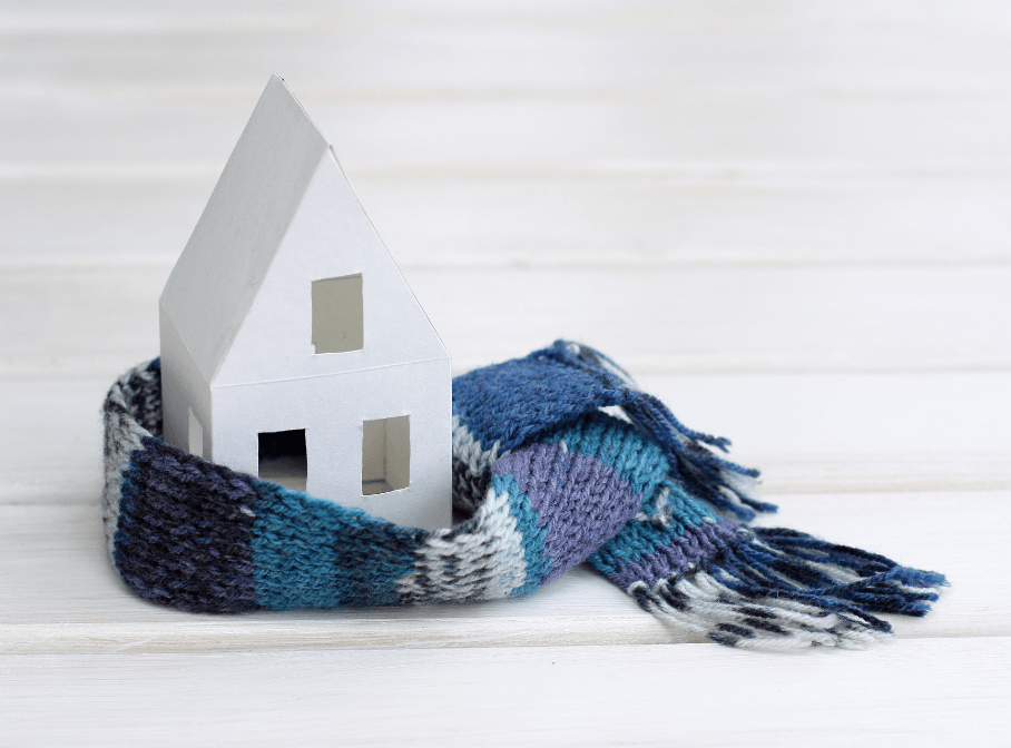 Image of a small white paper house sitting on a floor. There is a blue, green and black scarf wrapped around it to symbolize home insulation.
