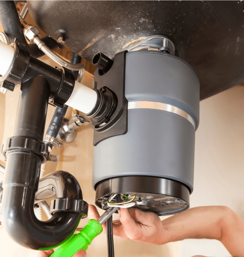Image of a garbage disposal from under the sink. You can see hands that are working on it with a screw driver.